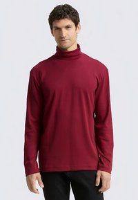 Burgundy turtleneck shirt made of soft, stretchy fabric. Long sleeves with a fitted design, featuring a raised collar.