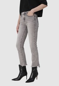 Jeans skinny gris avec un ourlet effiloché, dotés de poches avant et d'un design classique à cinq poches, associés à des bottines noires à talons pointus.