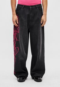 Schwarze, weite Denim-Hose mit auffälliger pinker Stickerei auf der linken Seite, traditionellem Fünf-Taschen-Design und Reißverschluss.