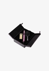 Outil de coiffure violet, brosse plate noire et produit doré dans une boîte noire texturée avec un intérieur en velours, s'ouvrant largement pour un accès facile.