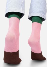 Kolorowe skarpetki mają różową część, zielony pasek na górze oraz brązowy ściągacz, wykonane z miękkiego, elastycznego materiału.