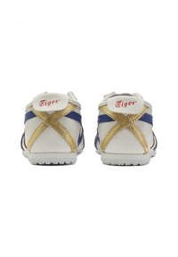 Sneaker in pelle bianca con accenti blu, fascia incrociata dorata e dettagli del logo rosso sul retro. Suola piatta in gomma bianca.