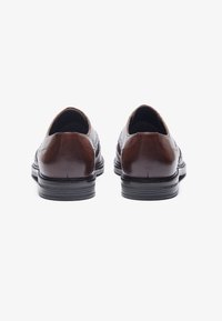 Bruine leren schoenen met een gladde afwerking, ronde neus en zwarte rubberen zolen; heeft minimale stiksels en geen zichtbare hardware.