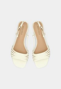 Sandales blanches à brides multiples horizontales, avec un bout carré et une semelle intérieure beige. Bride de cheville réglable avec un accent métallique.