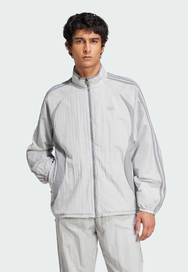Light gray windbreaker jacket with a high collar, front zipper, elastic cuffs, and three-stripe design down the sleeves. Features crinkled texture.