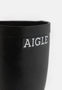 Botte en caoutchouc noir au fini mat, présente un logo AIGLE bien en vue en blanc sur un panneau noir. Design à bords ronds.