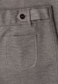 Zak van een grijze stoffen broek met een zwarte knoop bevestigd aan een versterkte riemlus, met gedetailleerde stiksels en een gestructureerd materiaal.