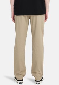 Beige pants with a relaxed fit, made of cotton, featuring a smooth texture, straight legs, and styled with black shoes.