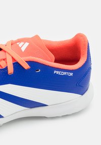 Chaussure de football synthétique bleue avec des accents orange vif, des rayures blanches, une tige texturée et un col intérieur rembourré. Logo "PREDATOR" visible.