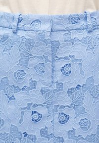 Υφασμα δαντέλας σε ανοιχτό γαλάζιο με λουλουδάτα σχέδια και ένθετα από δίχτυ, σχηματίζοντας έναν περίπλοκο, συμμετρικό σχεδιασμό στη μέση ενός ενδύματος.