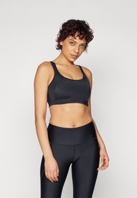 Svart sports-bh med brede stropper, sømløs design og en tettsittende fasong. Kombinert med høytlivs svarte leggings i et glatt, elastisk materiale.