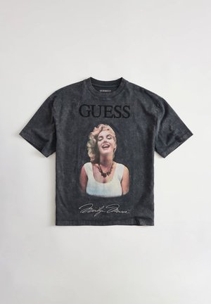Zwart Guess T-shirt met een glimlachend portret van Marilyn Monroe met halsketting, "GUESS" tekst erboven en haar handtekening eronder.