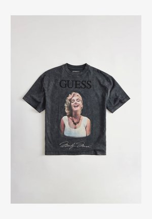 Zwart Guess T-shirt met een glimlachend portret van Marilyn Monroe met halsketting, "GUESS" tekst erboven en haar handtekening eronder.