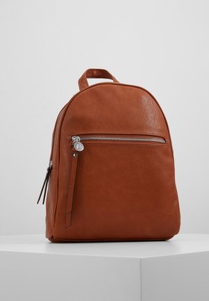 Brązowy skórzany plecak z przednią kieszenią na zamek i górnym uchwytem, prezentowany na białym piedestale na tle szarej ściany.