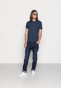 Marine t-skjorte, mørkeblå denimjeans og hvite sneakers. Antrekket har et enkelt design med en klassisk passform og rullede ermer.