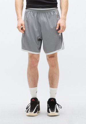 Grå atletiske shorts med elastisk midjebånd, lys kant og sidestreker. Brukes med hvite sokker og svarte sportsko.