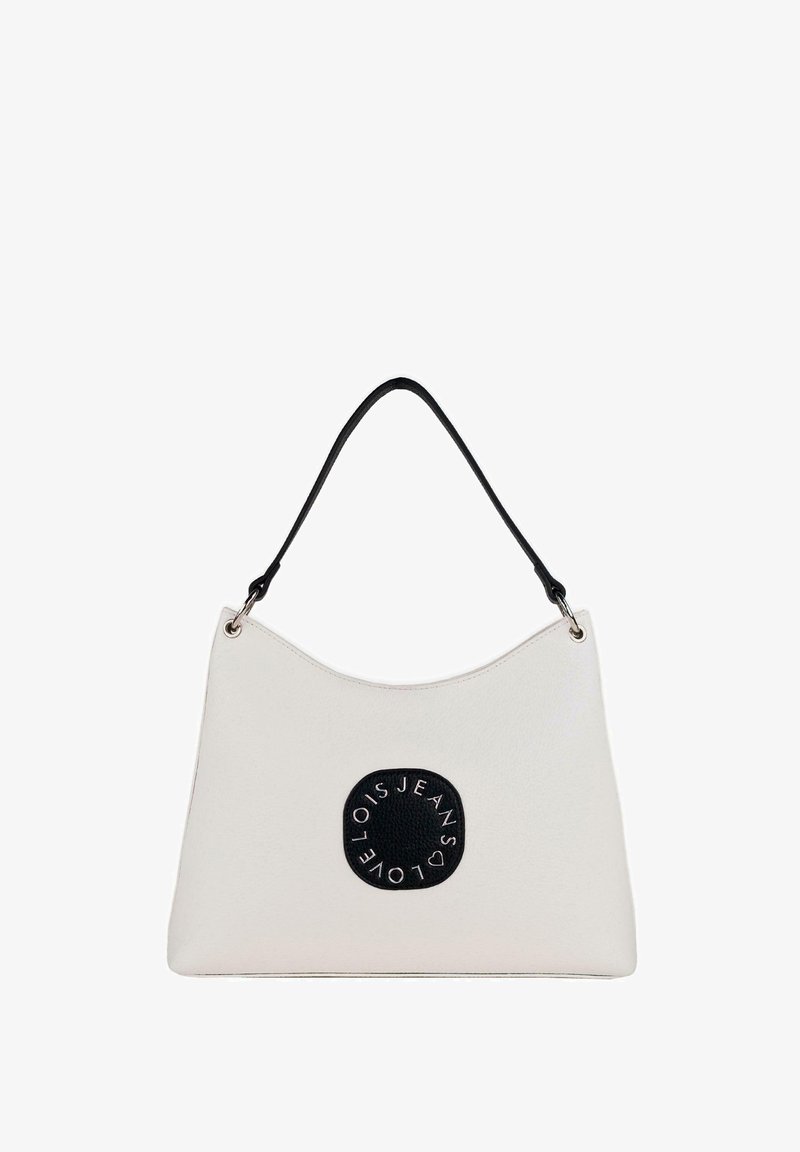 Bolso de hombro blanco de felpa con un diseño de parte superior curva, acentos en negro y un parche de logo circular prominente con detalles texturizados. Herrajes plateados visibles.