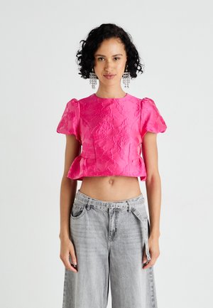 Pink cropped top with textured floral pattern, puffed sleeves, and a peplum hem paired with high-waisted, light gray wide-leg jeans.