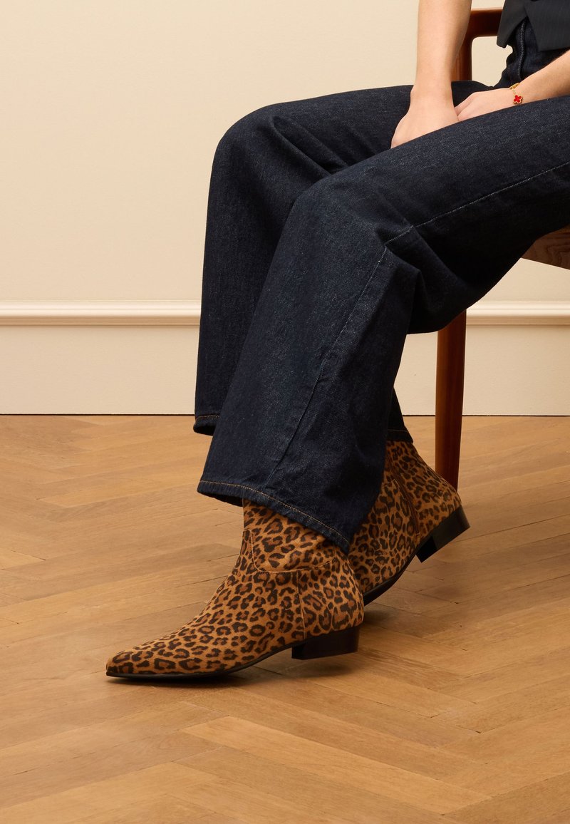 Stivaletti alla caviglia con stampa animale e punta affilata, realizzati in suede marrone, con tacco basso a blocco, indossati con jeans larghi scuri.