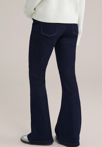 Vaqueros de campana azul oscuro en denim ligero con una textura suave y detalles de costura sutiles, que cuentan con bolsillos traseros y una altura media.