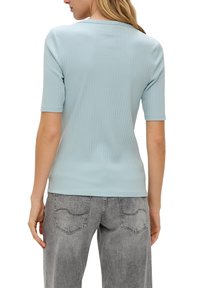 Lichtblauw geribd topje met korte mouwen, ronde halslijn en een gladde stofstructuur, gecombineerd met grijze jeans met patche pockets.