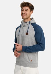 Šedá a námořnická mikina s kapucí, s klokankou, šňůrkou na kapuci a hnědou nášivkou loga na hrudi. Design s raglánovými rukávy.