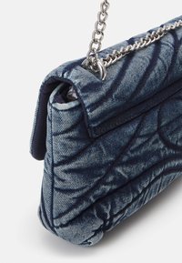 Borsa in denim con design trapuntato in blu scuro, dotata di tracolla in catena argentata e finitura morbida e testurizzata. Forma compatta con bordi arrotondati.
