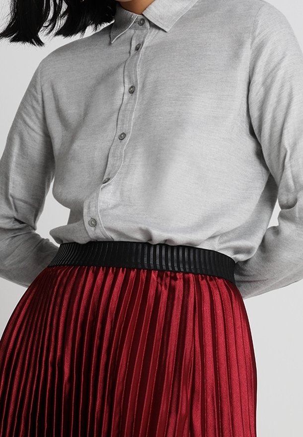 Grå skjorta med krage, kombinerad med en plisserad röd kjol med en svart texturerad midjeband. Slätt och glänsande tyg.
