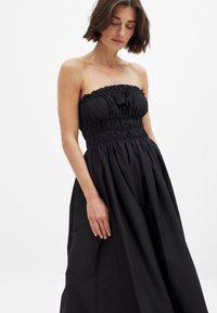 Robe noire sans bretelles avec un corsage froncé, une taille élastique et une jupe fluide. Fabriquée en tissu léger avec une texture douce.
