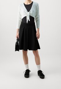 Světlomodrý pletený zkrácený kardigan s zavazováním vpředu, kombinovaný s černou áčkovou sukní. Model má na sobě černé platformové tenisky a bílé ponožky.