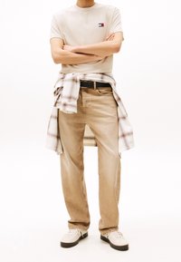 Beige puuvillane T-särk väikese logoga, millele on sobitatud heledast bežist denimist teksapüksid. Puuduv kootud särk on seotud vöö ümber. Valged tossud.