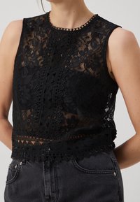 Top court en dentelle noire avec motifs floraux, col montant et bordure en dentelle délicate le long de l'ourlet. Porté avec un bas en denim foncé.