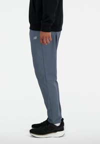 Grå træningsbukser lavet af let materiale med en slim fit design. Indeholder et diskret logo og er parret med sorte løbesko.