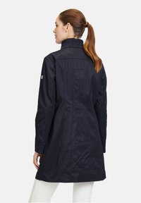 Manteau long bleu marine avec un col froncé, texture lisse et une poche arrière unique. Présente des manches longues et une coupe ajustée.