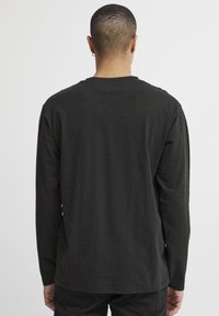 Black long-sleeve shirt made of soft fabric, featuring a crew neckline and a relaxed fit, with no visible patterns or hardware details.