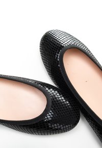 Bailarinas negras con un acabado texturizado y brillante, que cuentan con una plantilla rosa suave y un ribete elástico negro alrededor de la abertura.
