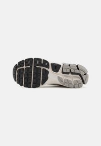 Suola di una scarpa da corsa con un battistrada in gomma nera a motivo, intersuola grigio chiaro con sezioni di ammortizzazione distintive e dettagli testurizzati.