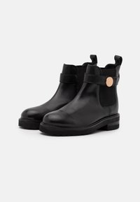 Bottes noires en cuir à la cheville avec une finition lisse, dotées de panneaux latéraux élastiques, d'une bride avec un accent métallique rond, et d'une semelle épaisse en caoutchouc.