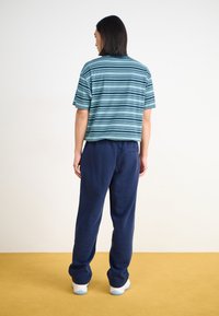 Τιρκουάζ και μπλε ριγέ κοντομάνικη μπλούζα σε συνδυασμό με ναυτικές φόρμες. Η μπλούζα έχει χαλαρή εφαρμογή και οι φόρμες διαθέτουν ελαστική μέση.