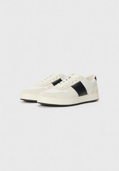 White and black sneaker, featuring a smooth leather upper, suede accents, round toe, and a textured sole. Classic lace-up design.