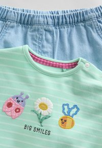 Lyseblå bukser med elastisk talje kombineret med en mintgrøn stribet top med applikerede smilende insekter, blomster og bier samt teksten "STORE SMIL".