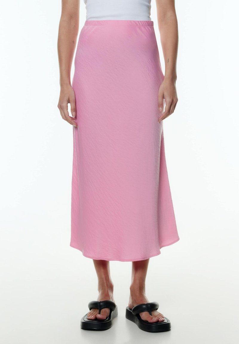 Roze, middellange rok met een gladde textuur en subtiele glans. Lichte stof valt zachtjes, met een rechte zoom en zonder zichtbare sluitingen.