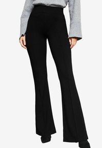 Pantalons évasés noirs en tissu extensible, dotés d'une taille haute et de détails de couture à l'avant, associés à un haut à manches longues gris.