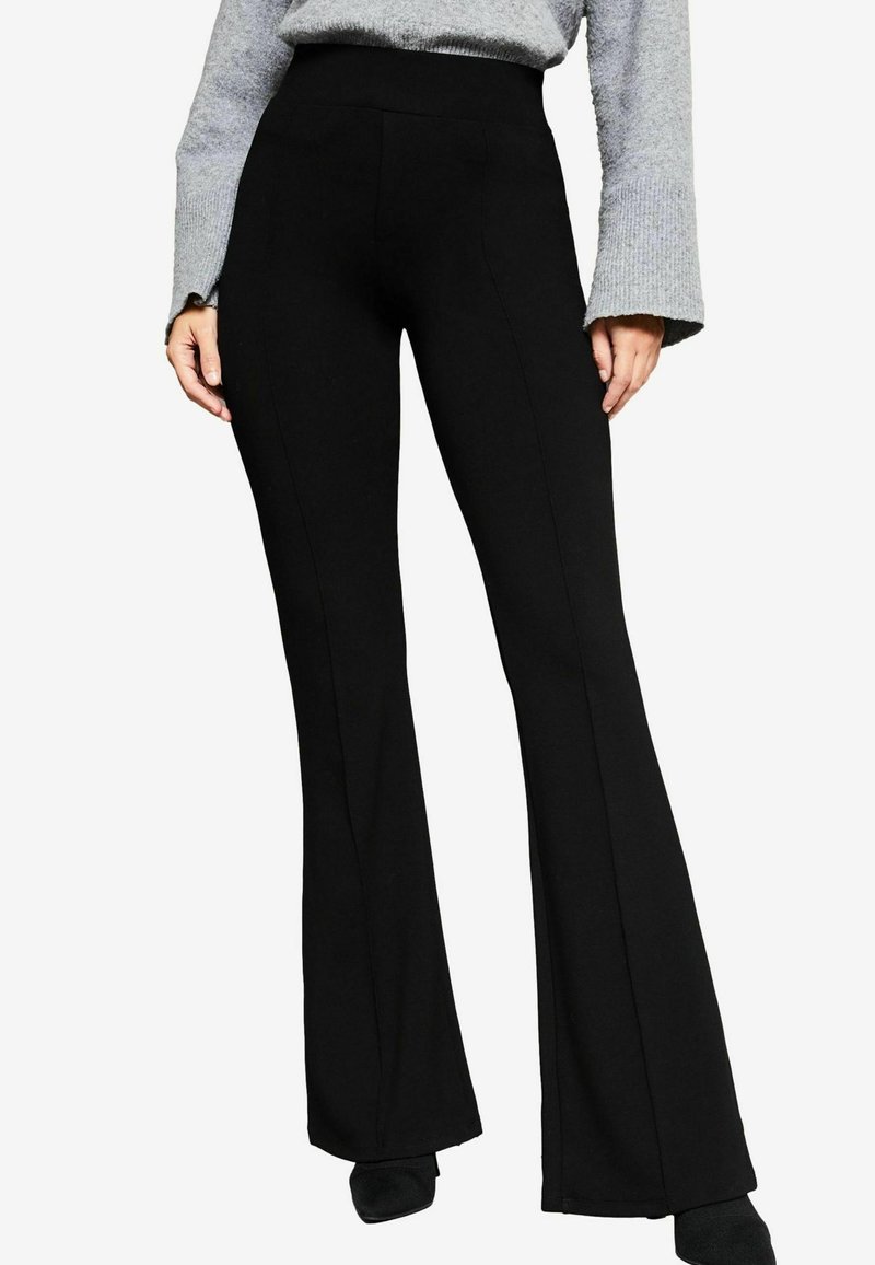 Pantalons évasés noirs en tissu extensible, dotés d'une taille haute et de détails de couture à l'avant, associés à un haut à manches longues gris.