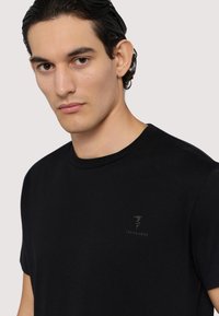 Svart t-shirt med rund hals i mjukt tyg, med en subtil präglad Trussardi-logotyp på bröstet. Kort ärm och normal passform.
