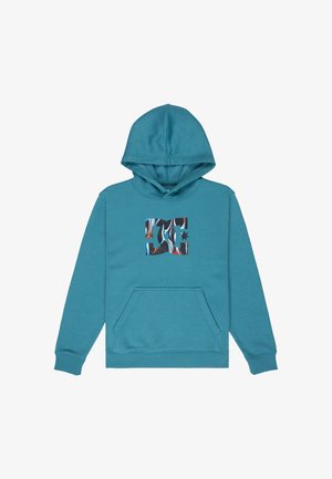 Blauer Kapuzenpullover mit einem grafischen Logo auf der Vorderseite, kombiniert mit Jeansshorts und schwarzen, weißen und roten Turnschuhen.