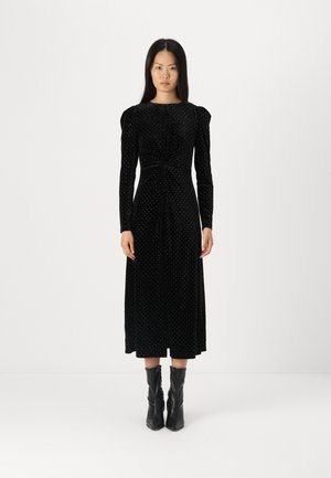 Svart fløyelskjole med lange ermer, knyttet midje-design og hvite prikker; midt på leggen, parret med svarte ankelboots.