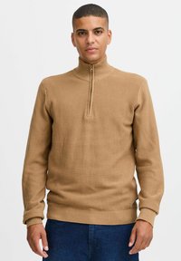 Brauner Strickpullover mit hohem Kragen und halbem Reißverschluss. Verfügt über ein strukturiertes Muster sowie gerippten Bündchen und Hüftbund. Aus weichem Material.