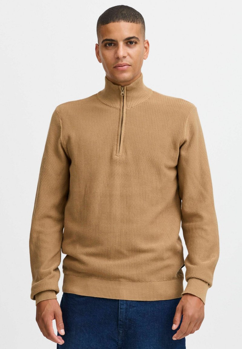 Brauner Strickpullover mit hohem Kragen und halbem Reißverschluss. Verfügt über ein strukturiertes Muster sowie gerippten Bündchen und Hüftbund. Aus weichem Material.
