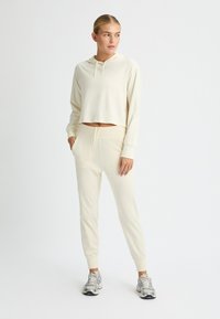 Lys beige cropped hoodie med en snoretræk hætte, parret med matchende tapered joggers med elastisk talje og sidelommer.